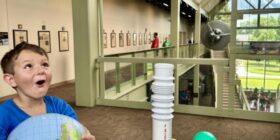 A group of children and adults sit in a planetarium, looking up with wide smiles and expressions of excitement as they look at an exhibit. The boy holds a globe and is enjoying this field trip with the Boys & Girls Clubs of Central and Northern New Hampshire.