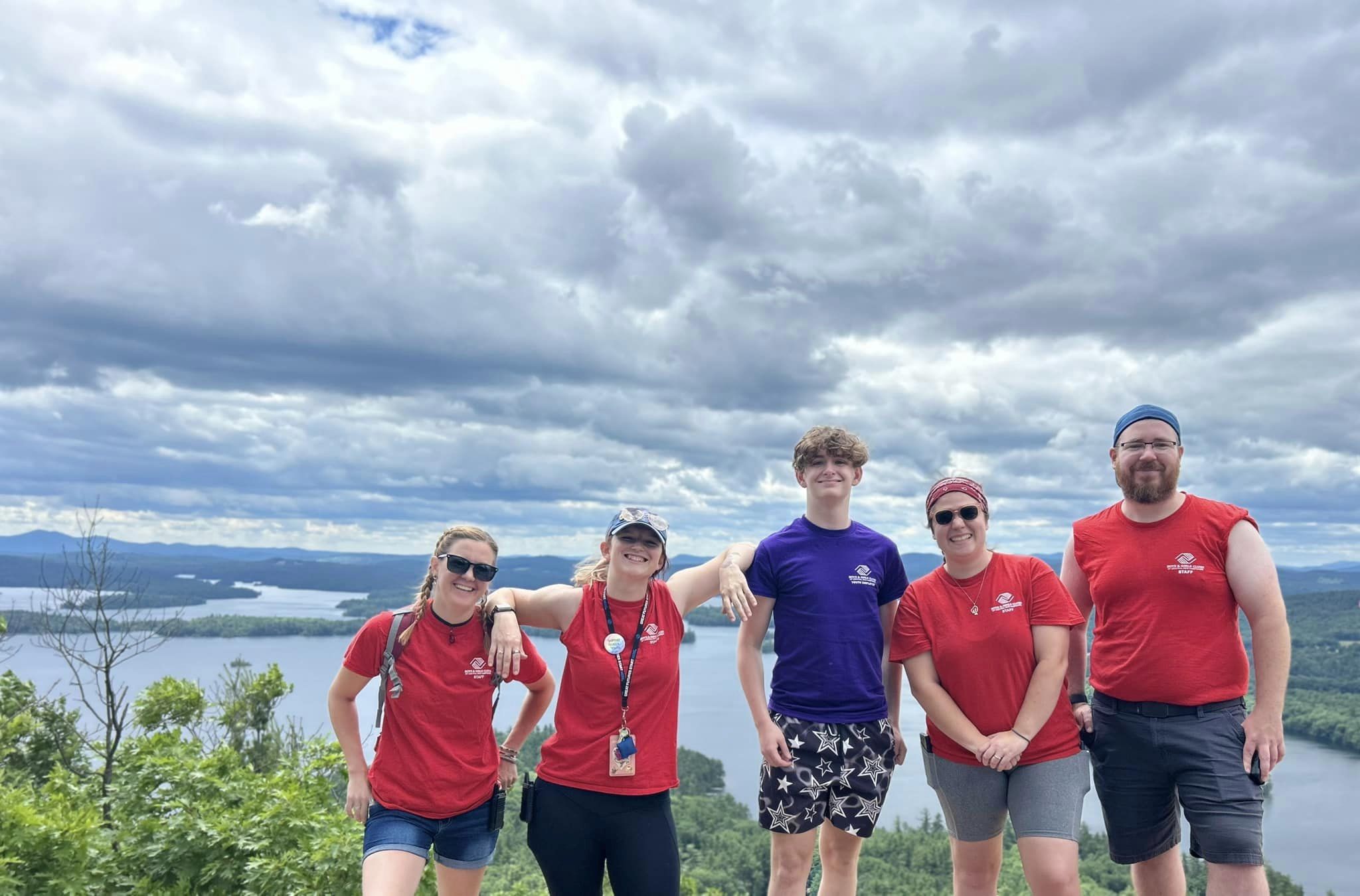 Five staff members from the Boys and girls clubs of central and northern new hampshire stand on top of a mountain in New Hampshire. They are smiling and enjoying beautiful scenery and nature.