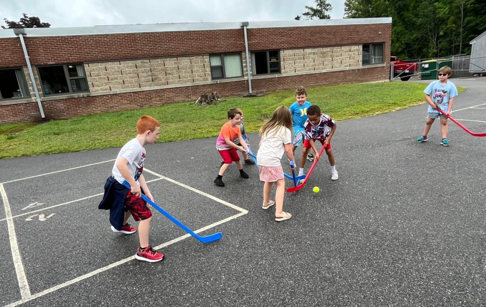 Pleasant St 4 group of children of mixed genders playing street hockey outside a school
