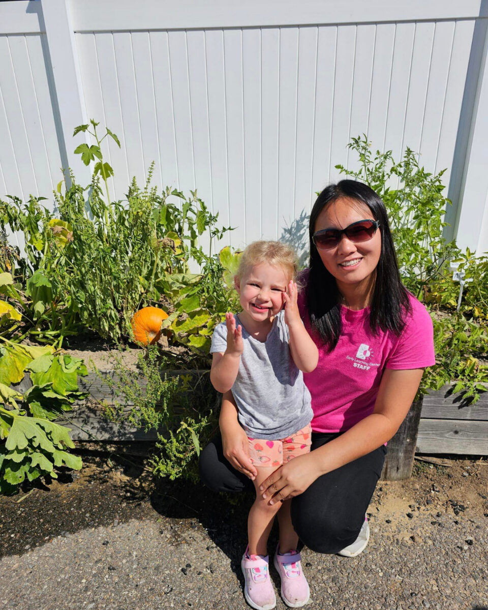 Staff member with a preschool child in front of the garden they grew together